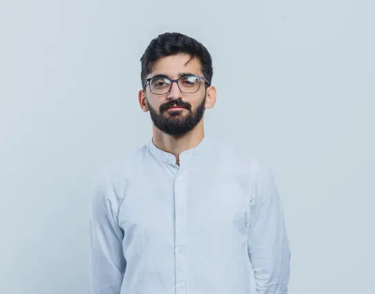 Indian man with glasses and beard wearing light blue shirt looking with confidence